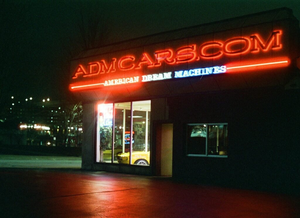 Millennials Car Buying Trends Reshape Automotive Finance 2025 Night view of a neon-lit car dealership in Des Moines, Iowa, USA.