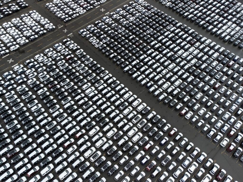 Auto Loan Application Rejections Are Plummeting in 2025—Here’s What to Watch Aerial perspective of an organized car parking lot with rows of vehicles arranged in a grid pattern.