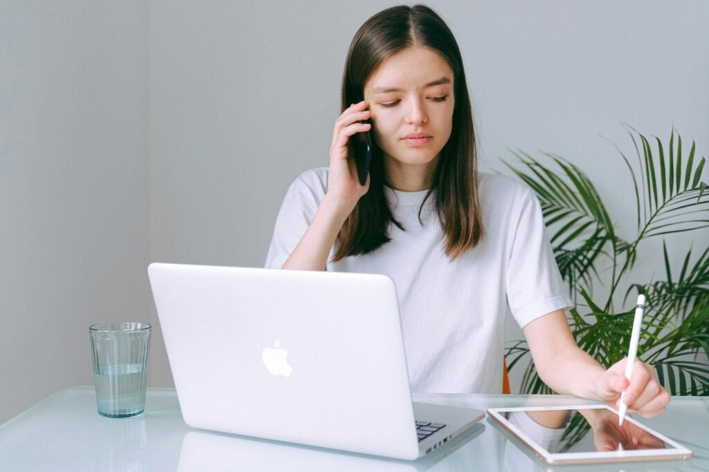 Millennials Car Buying Trends Reshape Automotive Finance 2025 A young millenial woman multitasking with a phone, laptop, and tablet in a bright home office setting.