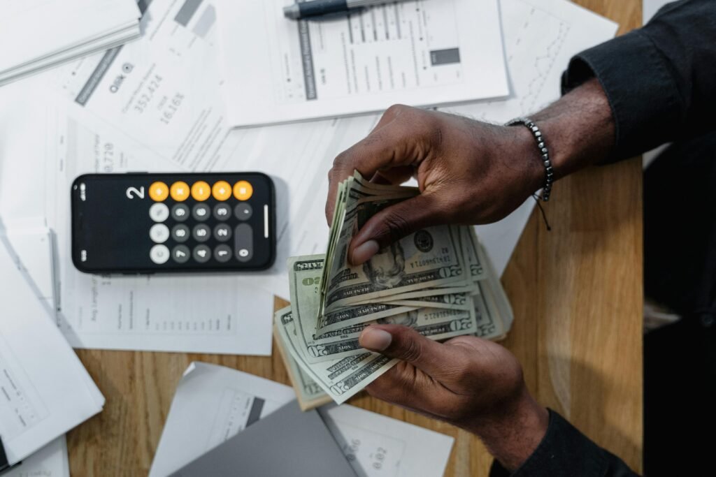 7 Answers to the Most Frequently Asked Questions About Automobile Person counting dollar bills over documents with a smartphone calculator on the desk.