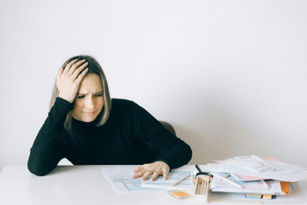 How 2025’s Affordability Crisis Affects Dealerships. Woman in black sweater stressed with financial paperwork, overwhelmed at white table.