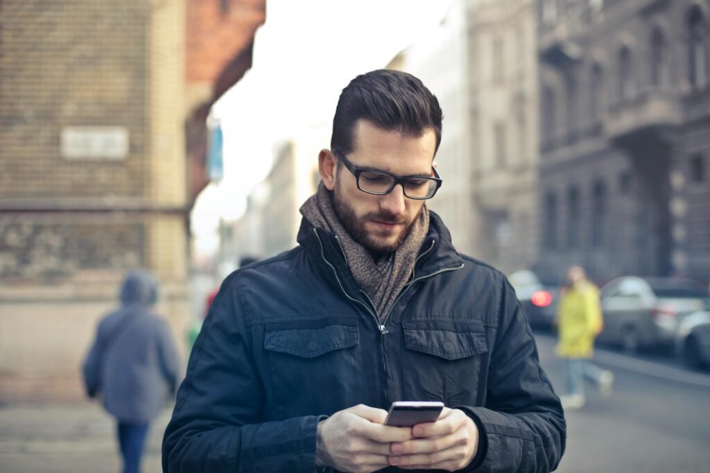 Millennials Car Buying Trends Reshape Automotive Finance 2025 Adult man with glasses using a smartphone on a city street in Budapest, Hungary.